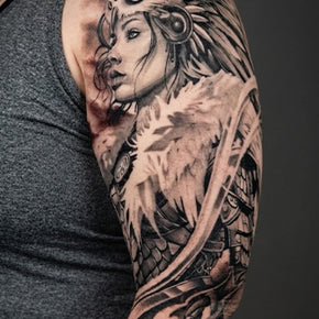 Black and grey tattoo of a warrior woman with feathers on a person's arm.
