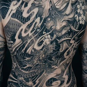 Intricate black and grey tattoo of a Japanese dragon and mask covering a person's back.