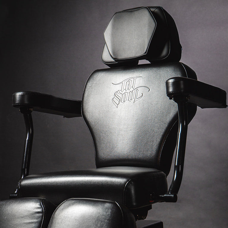 Black tattoo chair with armrests and engraved design on the backrest.