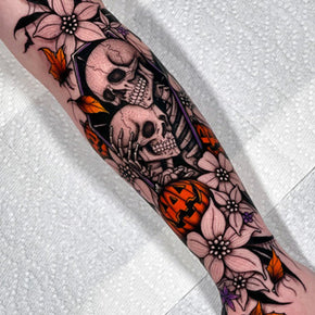 Coffin, skulls and pumpkin tattoo with flowers on a forearm.