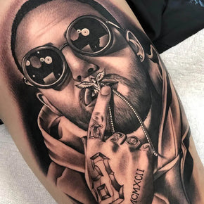 Tattoo of a man wearing sunglasses, holding a pendant with tattooed fingers.