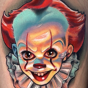 Tattoo of a colourful clown face with red hair and a ruffled collar.