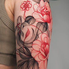 A black and red floral tattoo with koi fish and abstract elements on an upper arm.