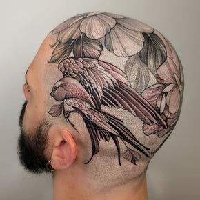 Bald man with a detailed tattoo of a bird and flowers on his scalp.