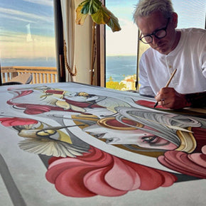 Artist painting a detailed artwork with red and gold elements.
