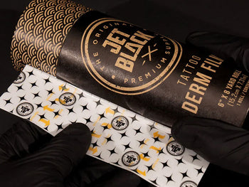 Gloved hands holding a roll of tattoo derm film with bold branding.