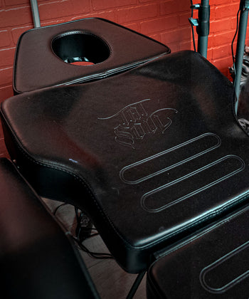 Tattoo chair with black leather padding and a face hole.