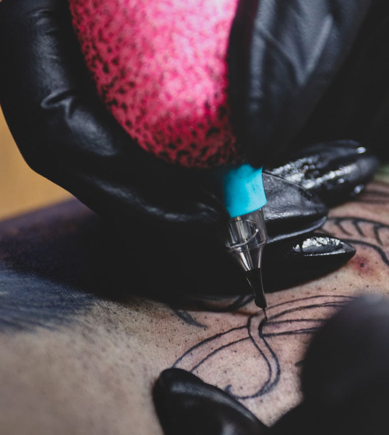 Tattoo artist wearing black gloves, inking a design on skin.