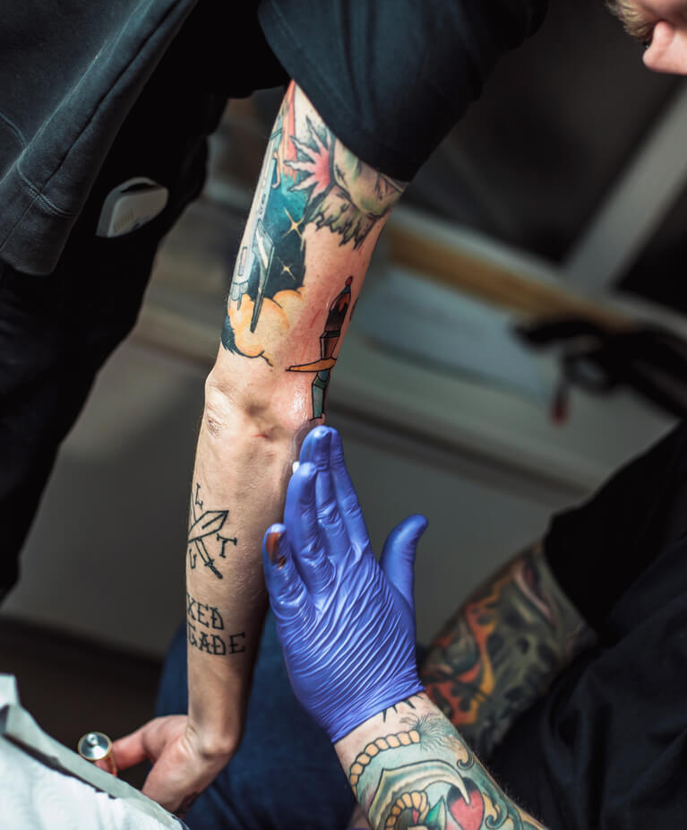Tattoo artist applying aftercare to a colourful tattoo on a person's arm.