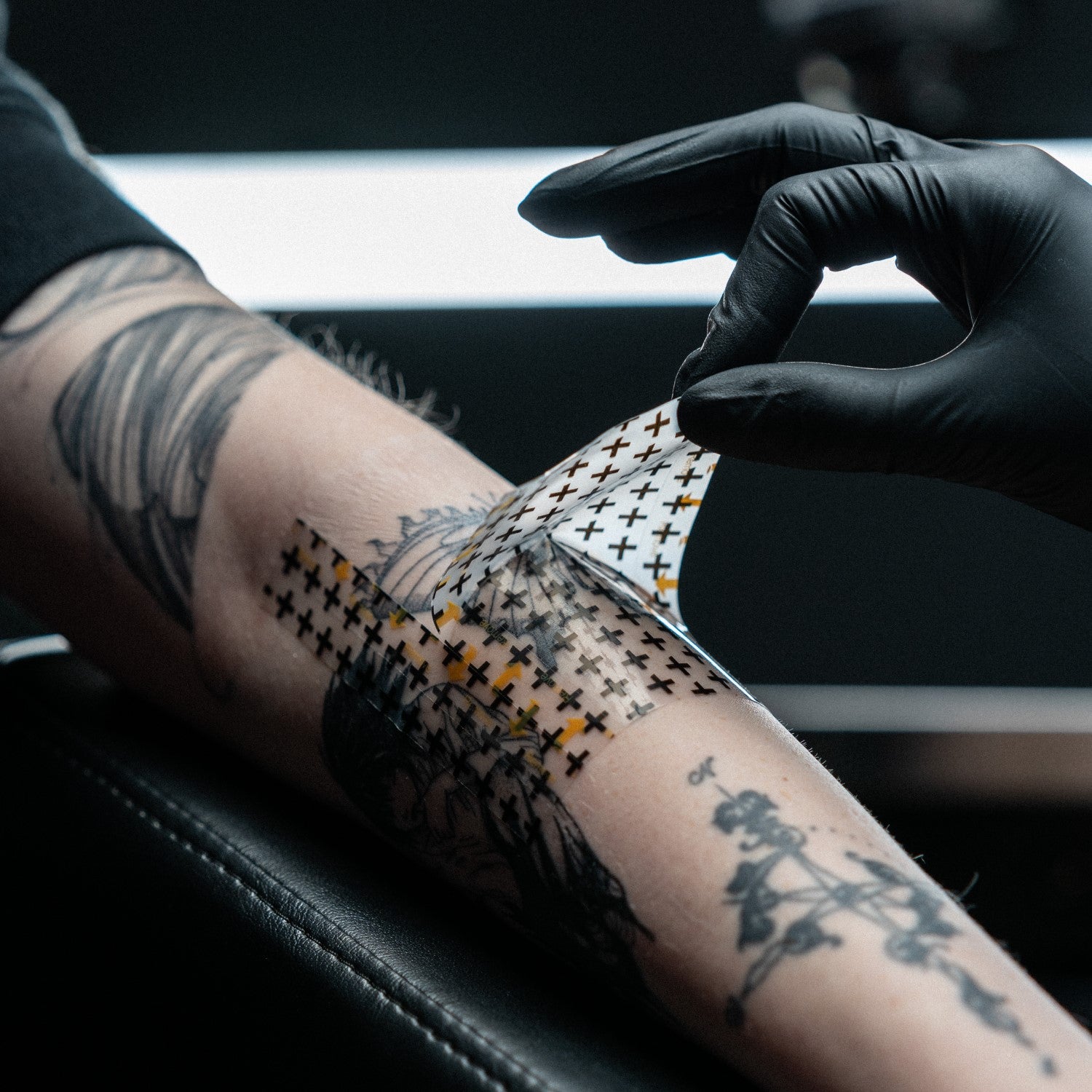 Tattoo artist removing a Recovery Derm Shield tattoo bandage applicator sheet off a new tattoo